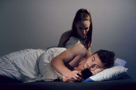 The concept of relationships and betrayal in the family. The man, lying in bed, corresponded with his mistress.の写真素材