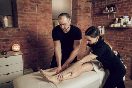 Two masseurs man and woman doing a foot massage to young woman. Young woman enjoying a massage in a spa salonの写真素材