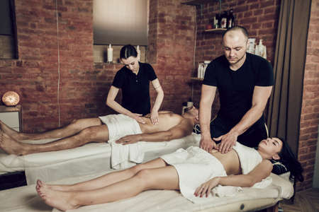 Two masseurs man and woman doing belly massage to a young couple. Man and woman lying on couches in spa. Spa treatments, therapeutic massageの写真素材