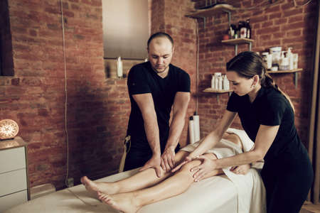Two masseurs man and woman doing a foot massage to young woman. Young woman enjoying a massage in a spa salonの写真素材