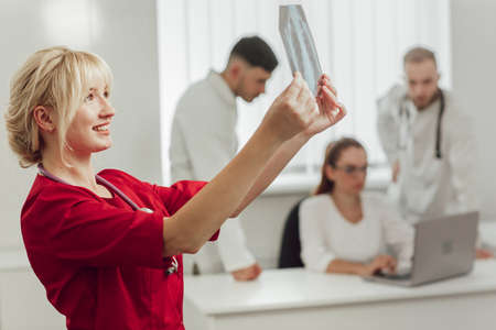 Young female doctor in hospital looking at x-ray. The other two doctors communicate in the...