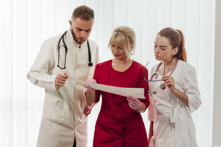 A team of four doctors standing in line at the clinic. Doctors read the patients tests. Medicine, treatment and health careの写真素材