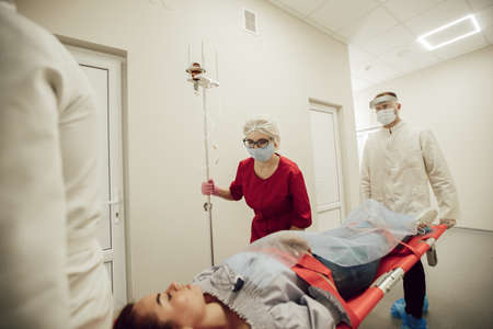 A team of doctors carry a sick patient on a stretcher. Ambulance doctors in protective masks and suits, the patient suspects coronavirus. The work of medics during a pandemicの写真素材