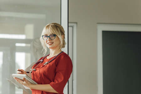 Close-up portrait of a young blonde doctor in a red uniform with a stethoscopeの写真素材