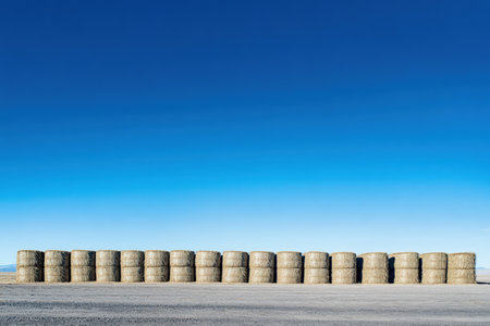 Row of hay bales stacked under a bright blue sky.の写真素材