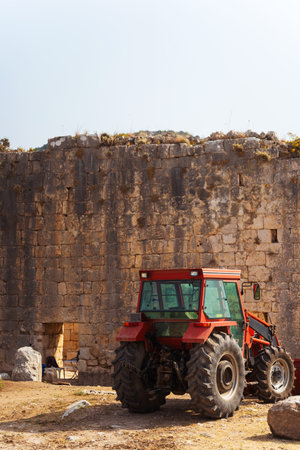 A red tractor is parked in front of a stone building and mountainsの写真素材