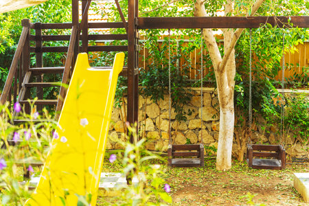 A wooden playground with a bright yellow slide and swings for kidsの写真素材