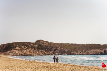 Couple walking along the seashore on sandy beach and rocksの写真素材