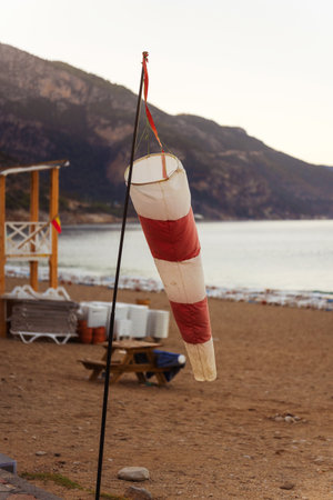 A colorful red and white wind vane is hanging from a tall pole on the beachの写真素材