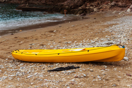 A bright yellow kayak is sitting on the sandy beach near the waterの写真素材