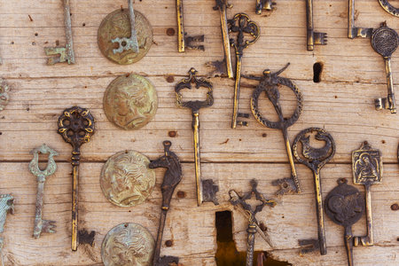 A collection of old and rusted keys are hanging on a wooden wall