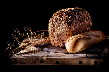 Brown bread and loaf of french bread on a dark background.