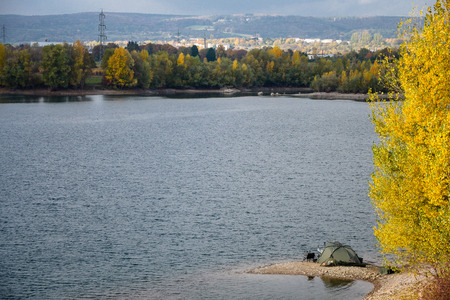 A calm autumn day, and the fisherman's tent spread on the edge of the lake. Yellow leaves of trees.の写真素材