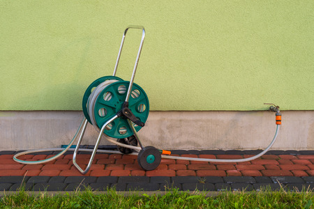 Garden hose connected to a green building facade.の写真素材