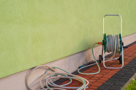 Garden hose connected to a green building facade.の写真素材