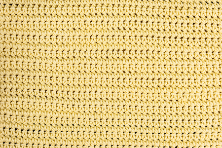 Real, yellow knitted fabric fragment made of wool fibers textured background, with delicate pattern.