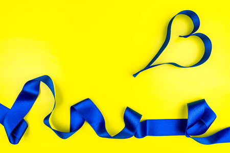 Heart made from blue satin ribbon on yellow background with copy space. Valentines Day concept.の写真素材