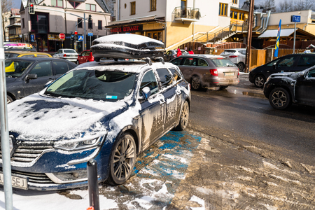 Zakopane, Poland - February 22, 2019. A dirty and snow-covered car standing in a parking lot on a busy, urban road. Photo taken in winter, urban buildings in the background.のeditorial素材