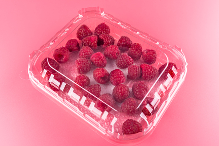 A lot of ripe raspberries in a closed, plastic package on a light pink background.の写真素材