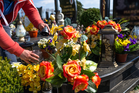 Artificial flowers and candlesticks lie on the tombstone, visible hands of a man.
