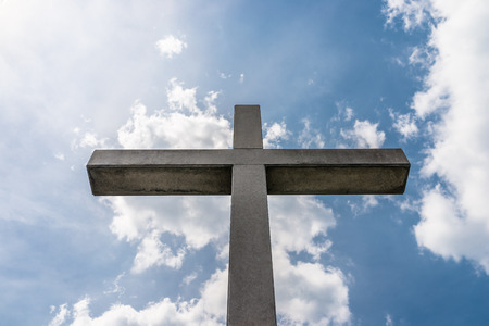 A large concrete cross against a blue sky with white clouds.の写真素材