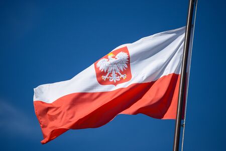 The state flag of Poland with the emblem of the Republic of Poland, on the background of the blue sky, in the wind.の写真素材