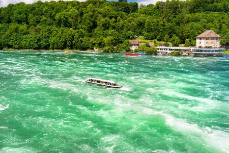 Neuhausen am Rheinfall, Switzerland - 23 July 2019. Waterfall on the river Rhine in Neuhausen am Rheinfall, Schaffhausen in Switzerland. Boats carrying tourists on the river near the waterfall.のeditorial素材