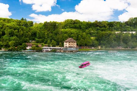 Neuhausen am Rheinfall, Switzerland - 23 July 2019. Waterfall on the river Rhine in Neuhausen am Rheinfall, Schaffhausen in Switzerland. Boats carrying tourists on the river near the waterfall.のeditorial素材