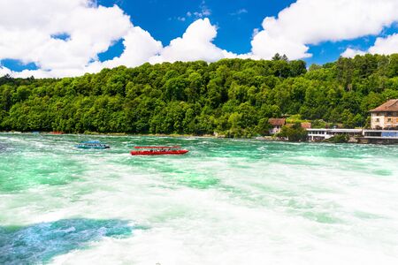 Neuhausen am Rheinfall, Switzerland - 23 July 2019. Waterfall on the river Rhine in Neuhausen am Rheinfall, Schaffhausen in Switzerland. Boats carrying tourists on the river near the waterfall.のeditorial素材
