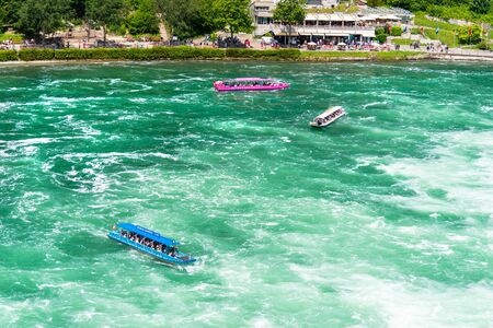 Neuhausen am Rheinfall, Switzerland - 23 July 2019. Waterfall on the river Rhine in Neuhausen am Rheinfall, Schaffhausen in Switzerland. Boats carrying tourists on the river near the waterfall.のeditorial素材