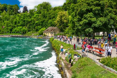 Neuhausen am Rheinfall, Switzerland - 23 July 2019. Waterfall on the river Rhine in the city of Neuhausen am Rheinfall in Switzerland.People walking and sitting on the promenade.のeditorial素材