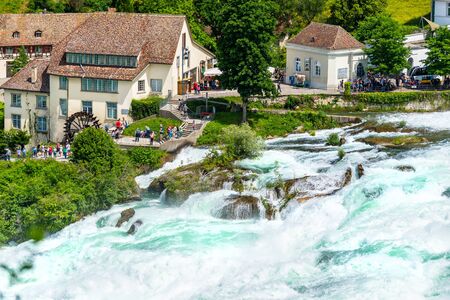 Neuhausen am Rheinfall, Switzerland - 23 July 2019. Waterfall on the river Rhine in the city of Neuhausen am Rheinfall in Switzerland.People walking and sitting on the promenade.のeditorial素材