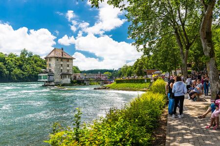 Neuhausen am Rheinfall, Switzerland - 23 July 2019. Waterfall on the river Rhine in the city of Neuhausen am Rheinfall in Switzerland.People walking and sitting on the promenade.のeditorial素材
