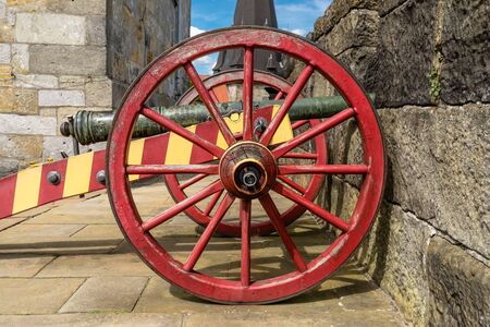 An antique cannon in a red-yellow color on the walls of a medieval castle.