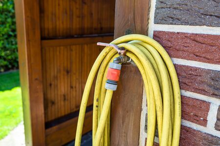 A garden yellow hose connected to a brick wall, a photo closeup.の写真素材
