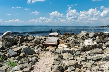 An old, wooden jetty over the beautiful Black Sea in Bulgaria, standing on a stony shore, in the background a sky with clouds.の写真素材