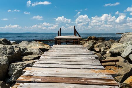 An old, wooden jetty over the beautiful Black Sea in Bulgaria, standing on a stony shore, in the background a sky with clouds.の写真素材