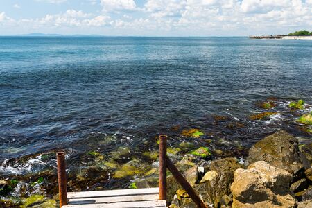 An old, wooden jetty over the beautiful Black Sea in Bulgaria, standing on a stony shore, in the...