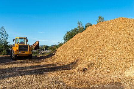 A large pile of wood chips lying on a square, with a blue sky in the background, visible bulldozer.の写真素材