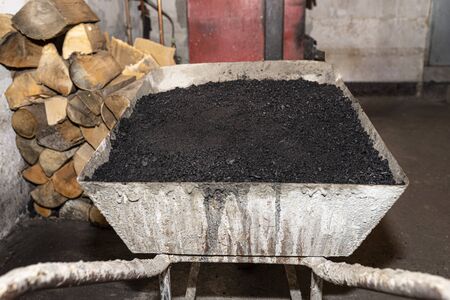 Wheelbarrow loaded with coal standing in the boiler room next to the furnace and firewood.