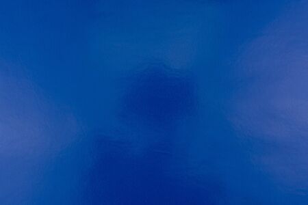 Blue background of real, shiny colored paper, illuminated by a soft light from above.