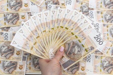 The woman is holding Polish banknotes on the front side, face value 200 PLN arranged in a fan, in the background a pile of Polish banknotes.の写真素材