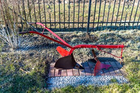 Traditional manual red plow made of steel, standing in the garden as an ornament.の写真素材
