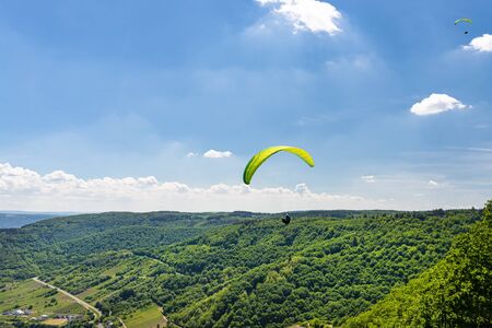 Man flying a green paraglider over beautiful wineries in Germany, visible river and forest.の写真素材
