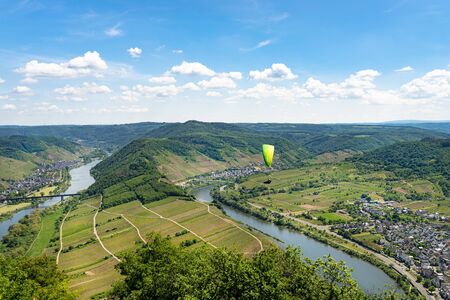 Man flying a green paraglider over beautiful wineries in Germany, visible river and forest.の写真素材