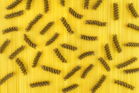 A dark green spiral pasta lying on a yellow background made of long yellow spaghetti pasta, top view.の写真素材