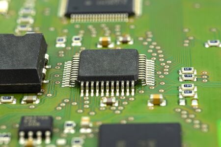 Macro photo of integrated circuit on a green circuit board, visible resistors and chip.