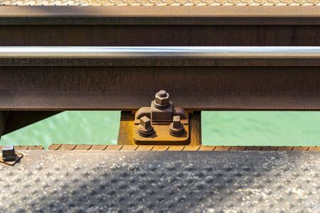 Railroad tracks located on the railroad bridge over the river, close-up on the fastening screw, lying on wooden sleepers, a turquoise river flows under the tracks.の写真素材