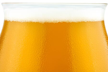 Macro shot of cold beer in a Teku tasting glass filled to full with foam, drops of water on glass,...