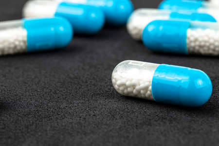 Blue gelatin capsules with white granules inside, isolated on a black background, macro shot.の写真素材